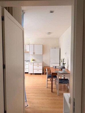 Una cocina moderna con armarios blancos, una mesa de comedor de madera y un refrigerador blanco.