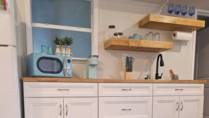 A kitchen with white cabinets, a microwave, and a sink. There are snacks and a remote control on the floor. - Breezy Loft at Palmetto, FL. (Palmetto)