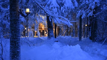 Schneebedeckte Landschaft mit einem Gebäude, das mehrere beleuchtete Fenster und einen sichtbaren Eingang hat.
