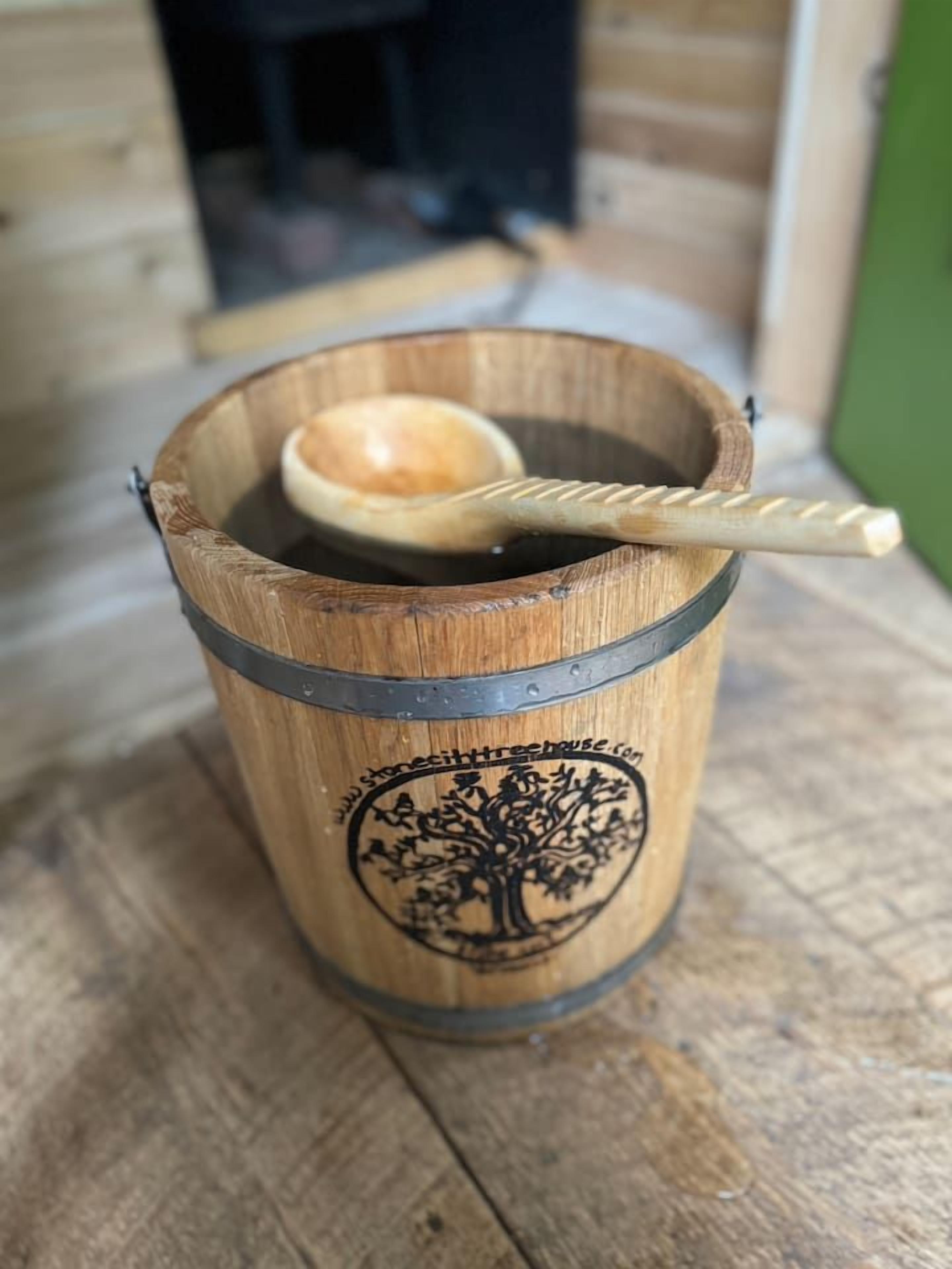 A wooden bucket with a metal band and a spoon inside, placed on a wooden surface.