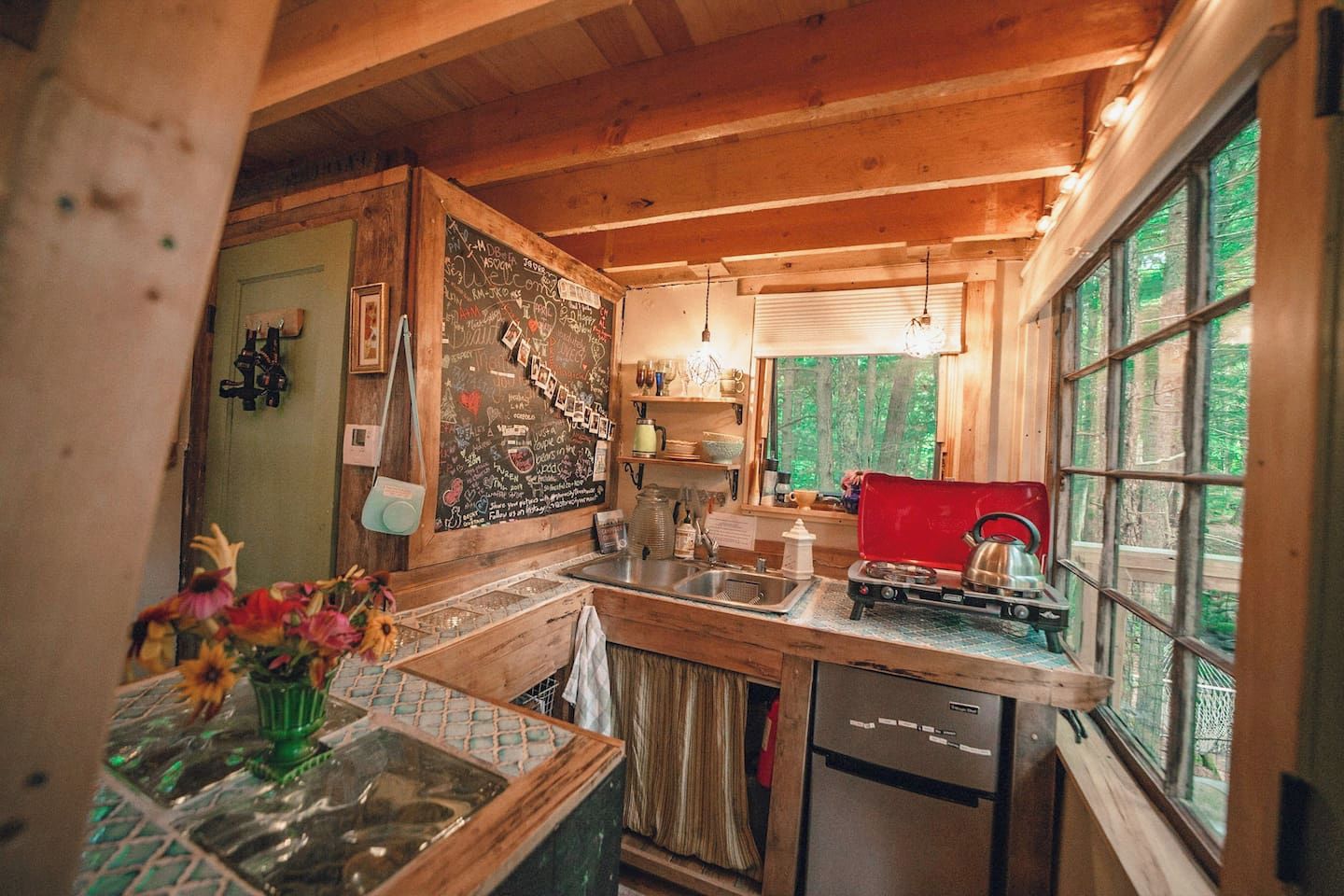 Eine gemütliche Küchenzeile in einer Holzhütte, mit einer Kreidetafel, einem Spülbecken und einem Fenster mit Blick auf einen Wald.