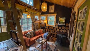 A cozy cabin interior with a wooden ceiling, a sofa, a small table, and a fireplace. - Streamside treehouse in the Vermont forest with access to sauna (Hardwick)