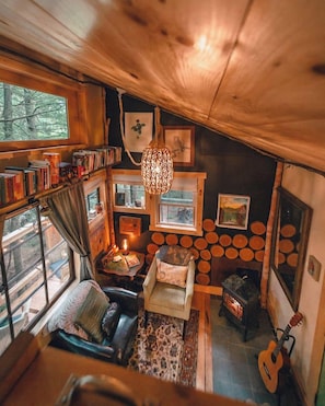 Interior acogedor de una cabaña con chimenea, estanterías, un rincón de descanso cómodo y una guitarra.