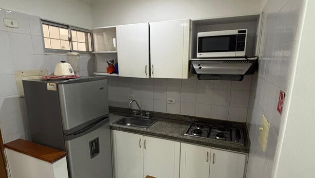A compact kitchen with white cabinets, a stainless steel refrigerator, a microwave, a gas stove, and a sink. - A few steps from the beach in El Rodadero (Santa Marta)