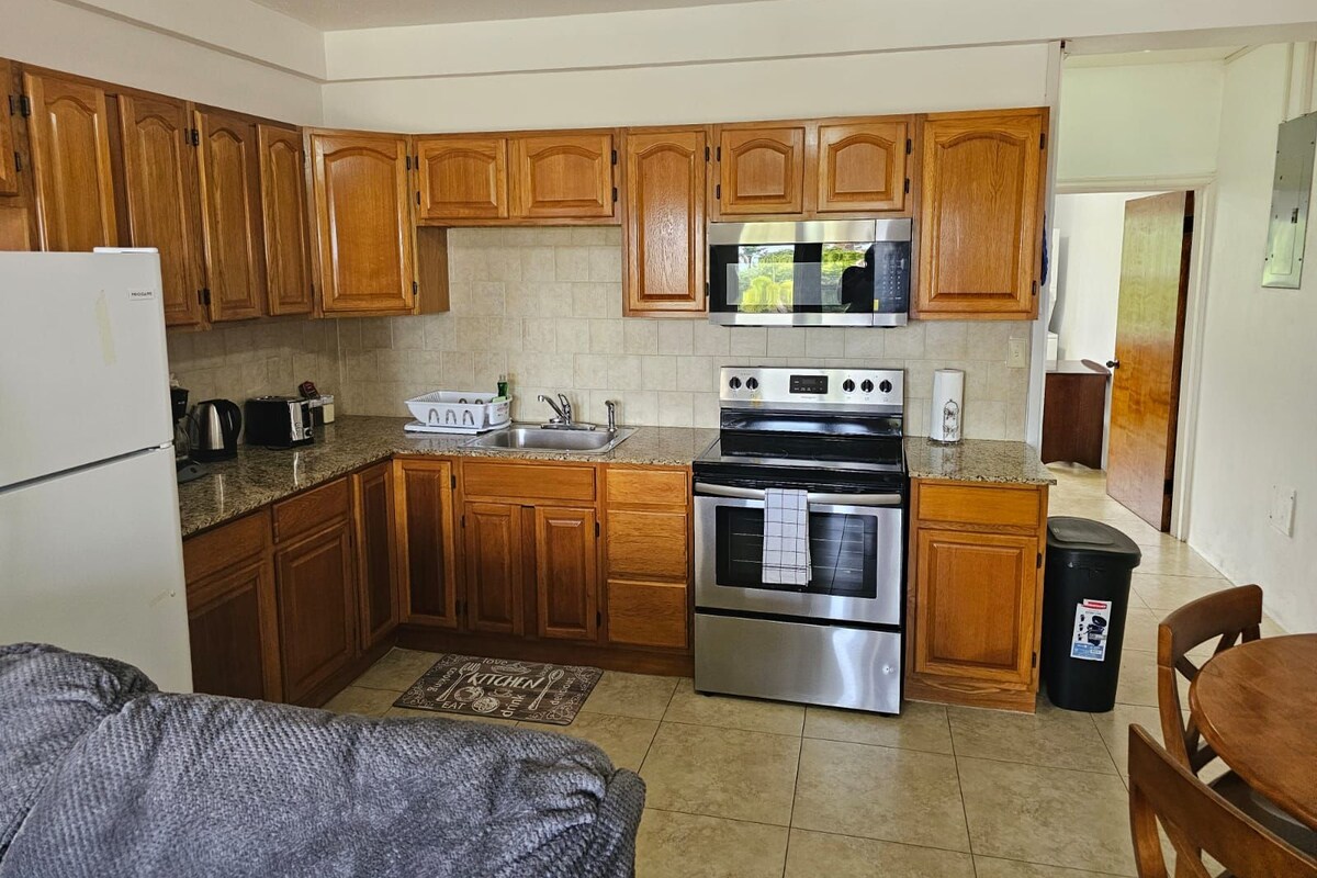 A compact kitchen with wooden cabinets, a stainless steel refrigerator, a microwave, a stove, and a sink.