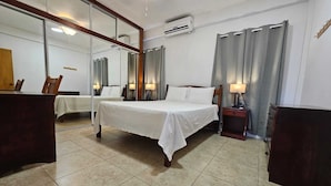 A hotel room with a bed, a nightstand, a mirror, a desk, and a chair. - Aurela Residences (St. John's)