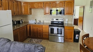 A compact kitchen with wooden cabinets, a stainless steel refrigerator, a microwave, a stove, and a sink. - Aurela Residences (St. John's)
