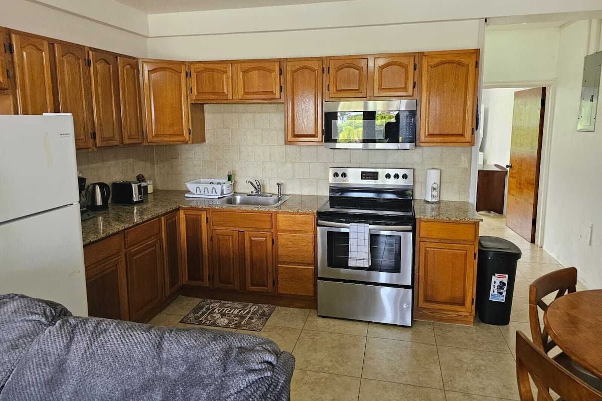 A compact kitchen with wooden cabinets, a stainless steel refrigerator, a microwave, a stove, and a sink.