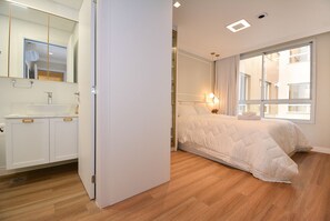 A modern bedroom with a large bed, a bedside table, and a window with curtains.