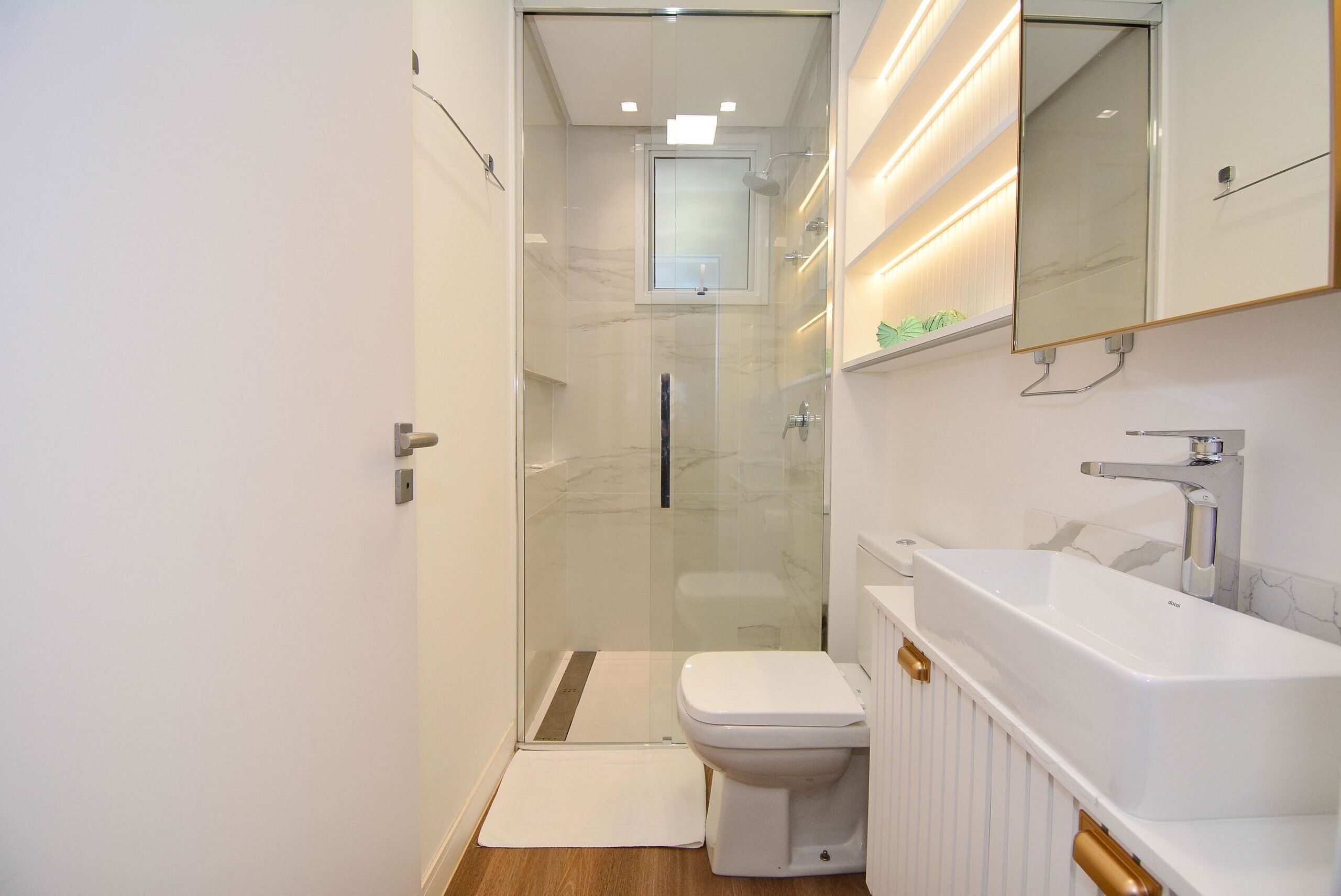 A modern bathroom with a glass-enclosed shower, a white toilet, and a white sink with a gold faucet.