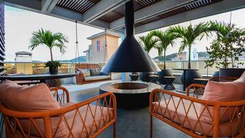 A rooftop terrace with wicker chairs, a round table, and a black conical structure.
