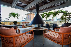 A rooftop terrace with wicker chairs, a round table, and a black conical structure.
