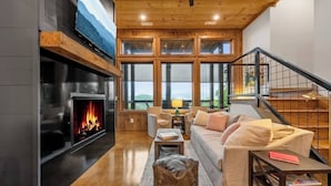 A cozy living room with a fireplace, a sofa, and a staircase. - Luxury Blackbird Cabin | Views, Hot Tub & Fire Pit (Blue Ridge)
