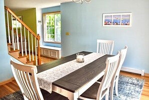 A dining area with a wooden table, white chairs, a patterned table runner, and a view of a staircase.