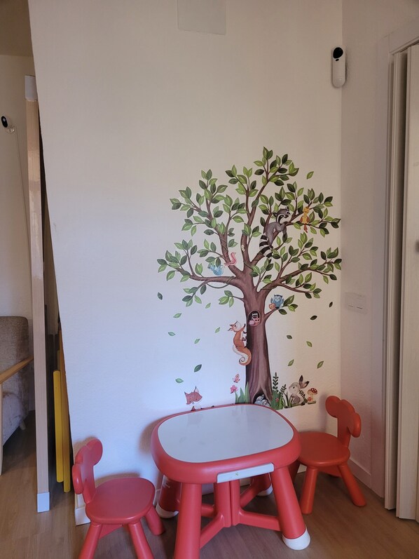 A room with a white wall featuring a tree mural, a small round table, and two red chairs.