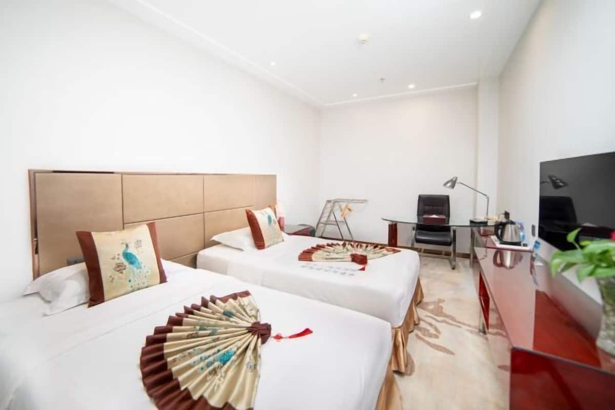 A hotel room with two beds, a desk, a TV, and a plant.