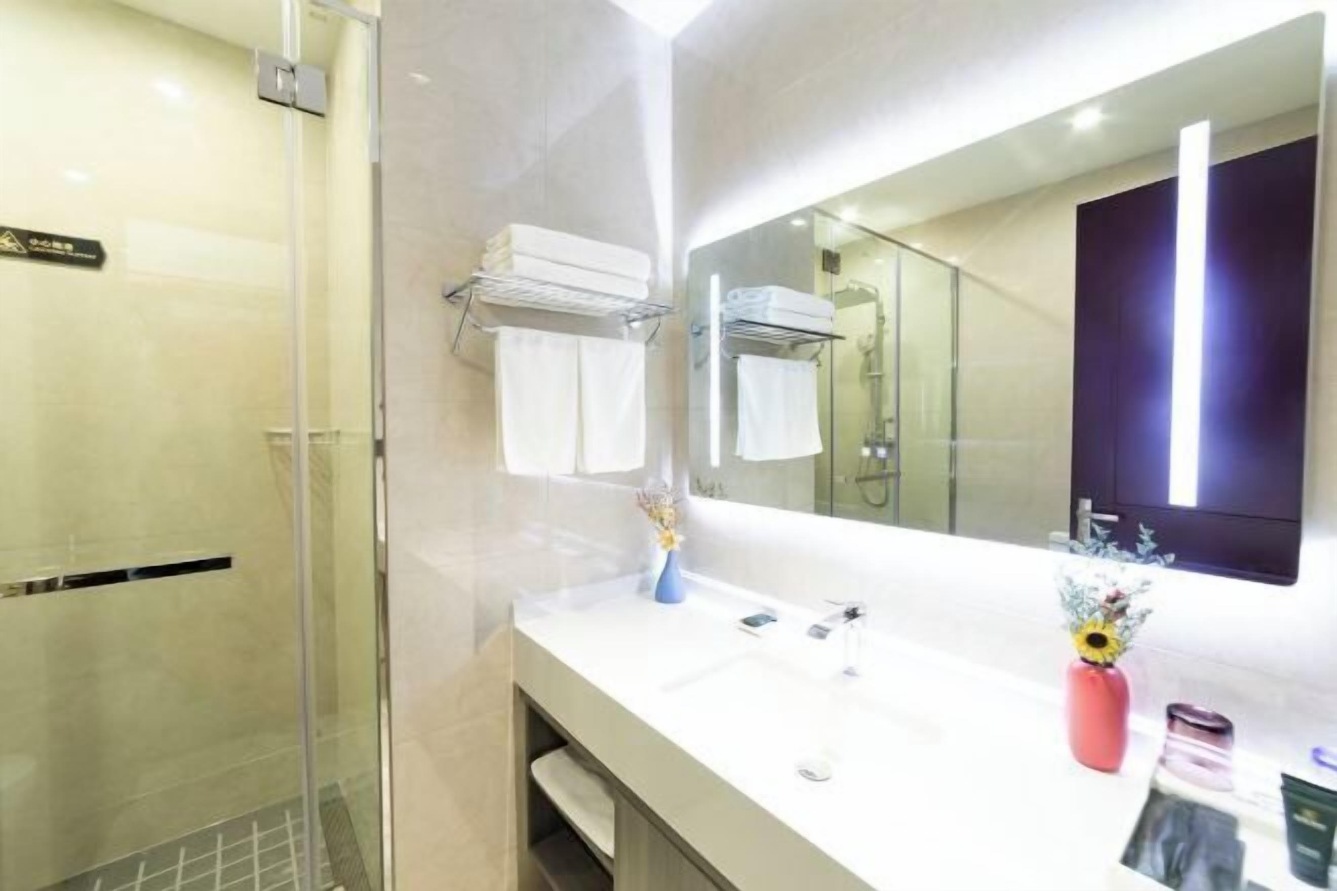 Een moderne badkamer met een glazen douchecabine, een witte wastafel, een grote spiegel en een handdoekhouder.