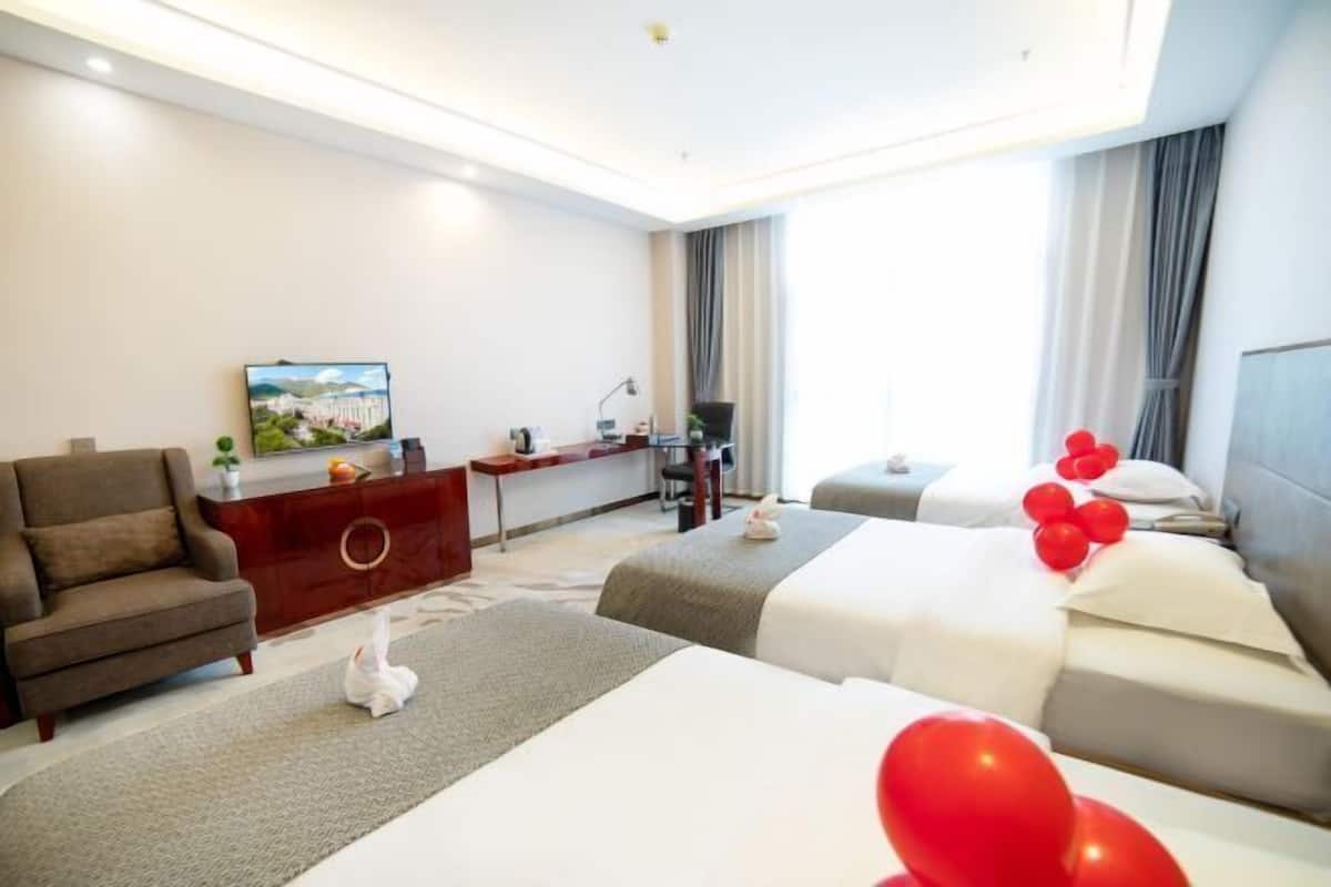 A hotel room with two beds, a sofa, a desk, a TV, and a painting on the wall.
