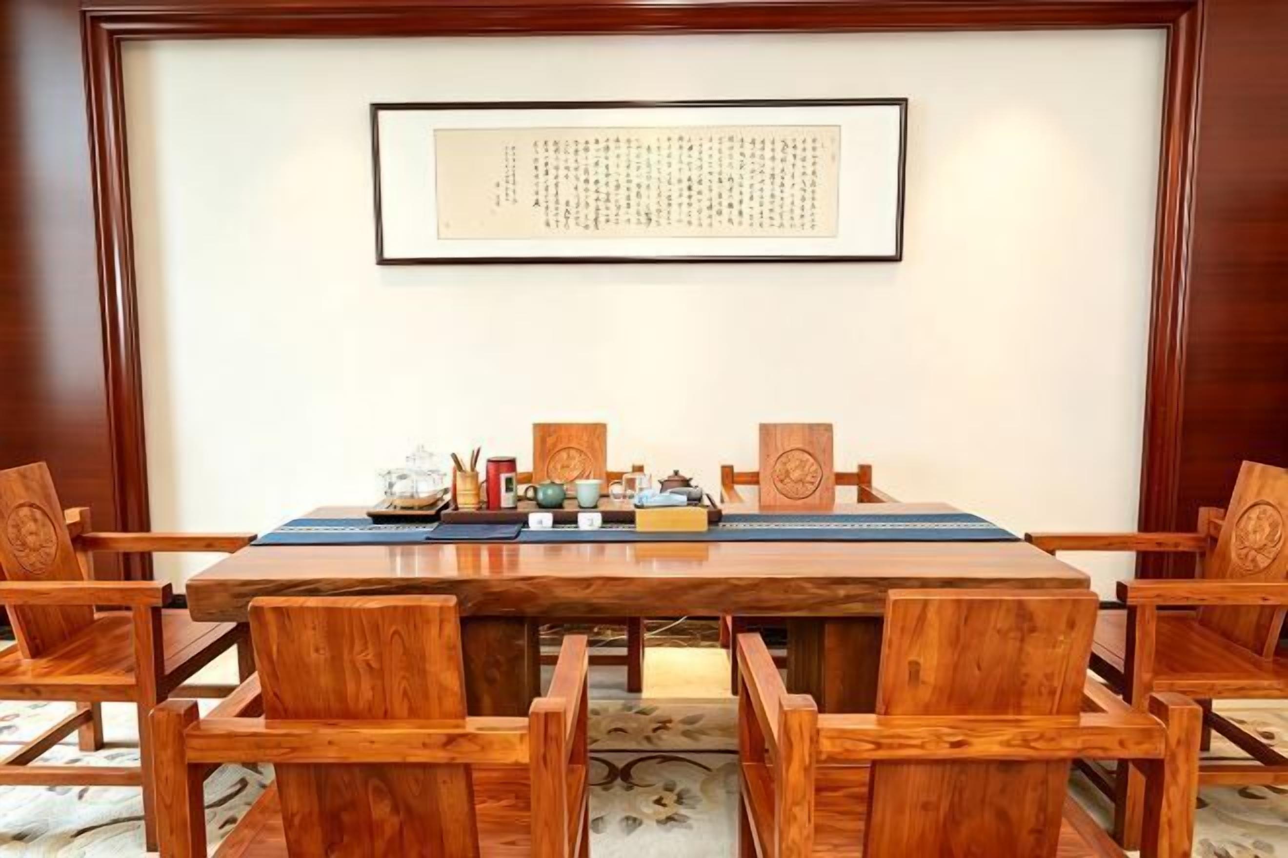 A conference room with a long wooden table, six chairs, and a framed document on the wall.