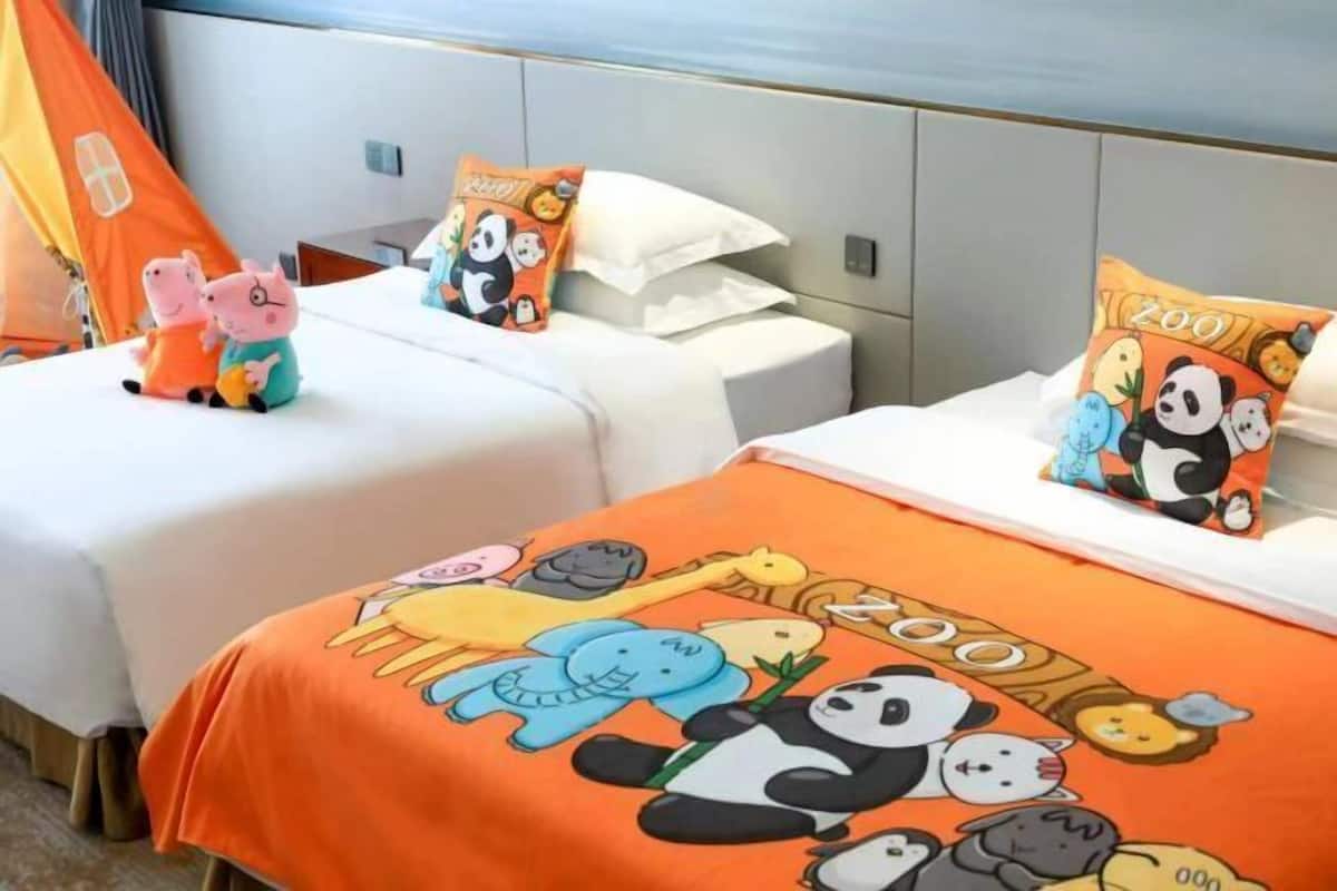A hotel room with two beds, each with a panda-themed pillow and a blanket.