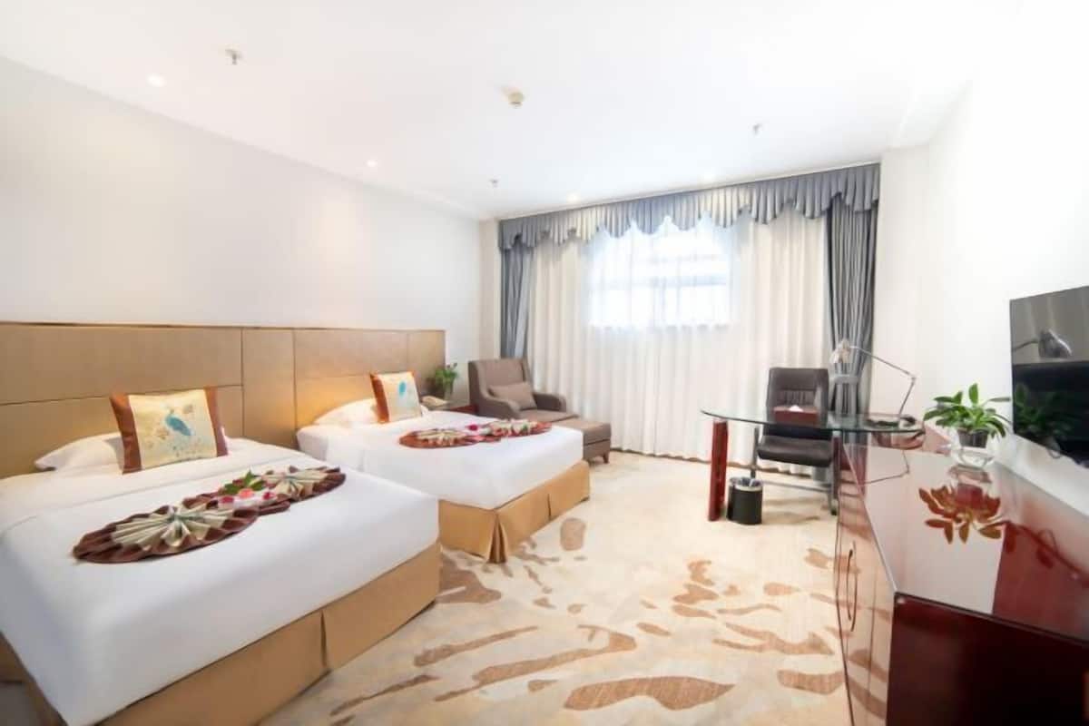 A hotel room with two beds, a desk, a chair, a TV, and a large window with curtains.