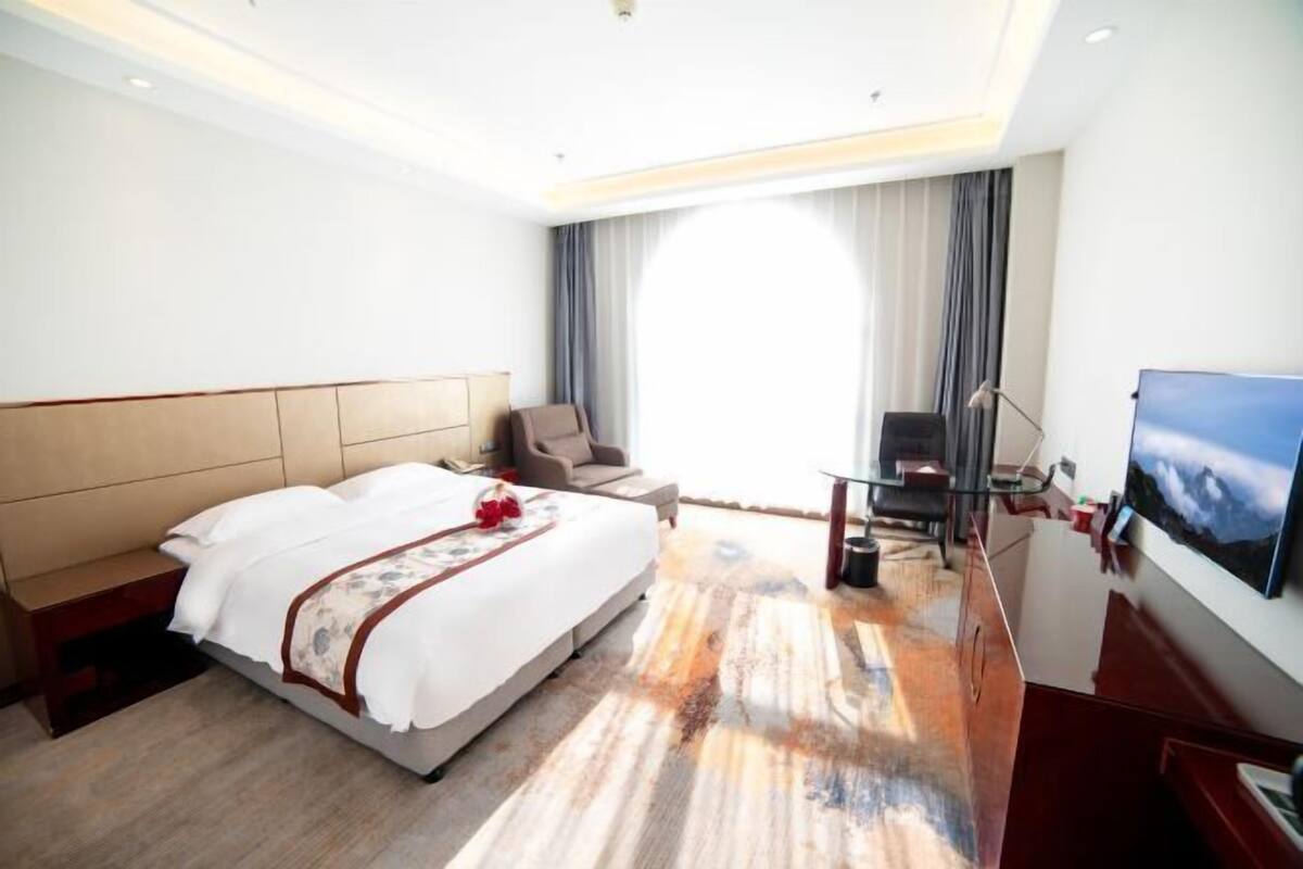 A hotel room with a large bed, a desk, a chair, a TV, and a view of the outdoors.