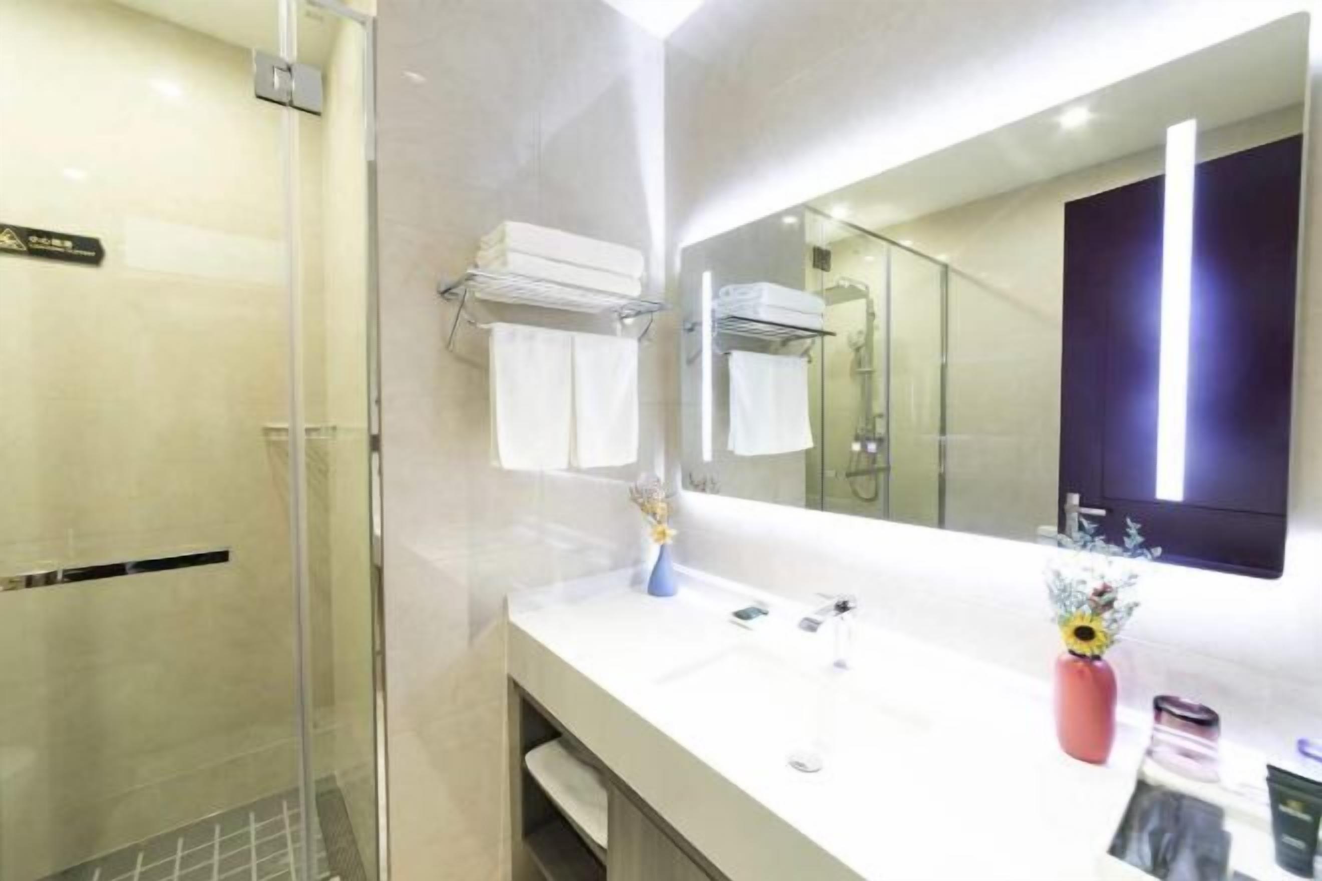 Une salle de bain moderne avec une douche à parois de verre, un lavabo blanc avec un miroir et un vase rempli de fleurs.