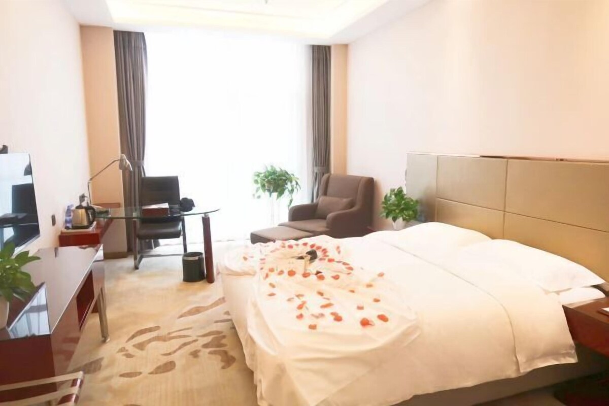 Une chambre d’hôtel avec un lit, un bureau, une chaise, une télévision et deux plantes.