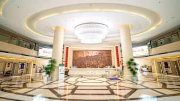 Um hall amplo com um grande candelabro, um balcão de recepção e um design de piso geométrico moderno.