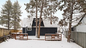 A snow-covered backyard with a wooden bench, a table, and a house in the background. - PureSky Cabin (Big Bear City)