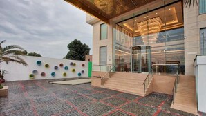 A modern building with a glass facade, a set of stairs leading to a revolving door, and a colorful wall art installation. - Country Inn Premier Amritsar (Amritsar)