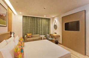 Habitación de hotel con una cama grande, un escritorio, un sofá y un televisor.