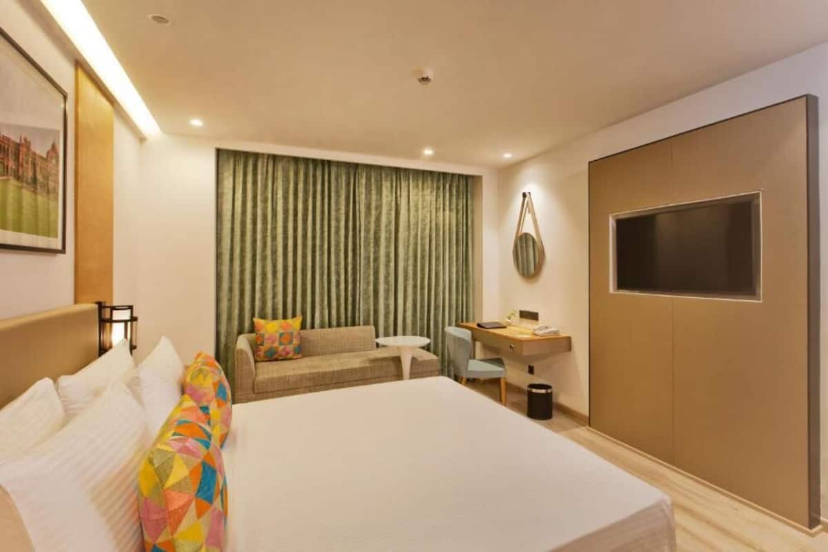 A hotel room with a large bed, a desk, a sofa, and a TV.