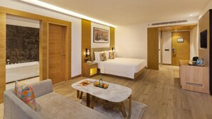 A modern hotel room with a bed, a sofa, a small table, and a bathroom with a bathtub. - Country Inn Premier Amritsar (Amritsar)