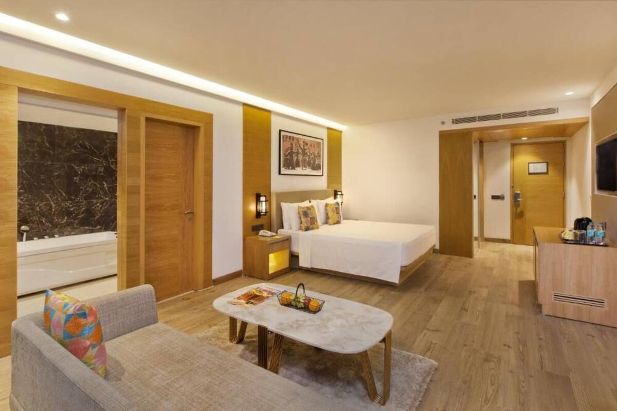 A modern hotel room with a bed, a sofa, a small table, and a bathroom with a bathtub.