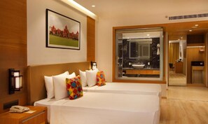 Habitación de hotel con dos camas, un espejo grande, un cuadro de un edificio y vistas al baño.