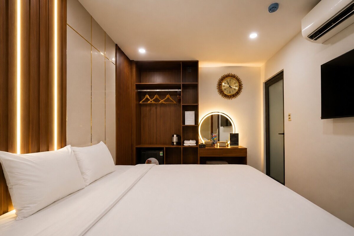 Ein Hotelzimmer mit einem großen Bett, einem Schminktisch mit Spiegel, einer Uhr und einem Kleiderschrank.