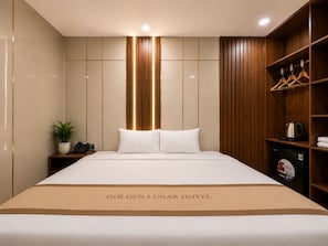 A hotel room with a bed, a nightstand with a phone and a plant, a wooden wardrobe, and a sign on the bed reading 'GOLDEN LUNAR HOTEL.' - Golden Lunar (Ho Chi Minh City)