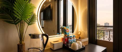 A modern bathroom with a round mirror, a coffee maker, a kettle, a plant, and toiletries on a counter.