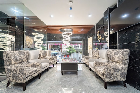 Un lobby moderno con suelo de mármol, dos sofás con tapicería floral, una mesa de centro y una lámpara colgante en espiral.