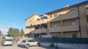 A multi-story residential building with balconies, a parking area, and a green fence. - Cleo Dalia (Ancona)