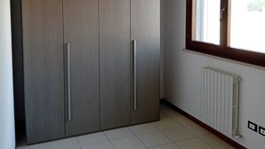 A room with a large wardrobe, a radiator, and a window with a view of greenery. - Cleo Dalia (Ancona)