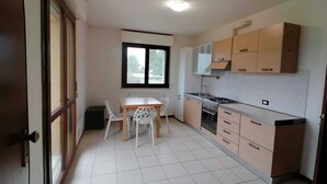 A compact kitchen with a dining table and chairs, a window, and cabinets. - Cleo Dalia (Ancona)