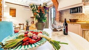 A dining area with a table set for two, featuring a plate of vegetables, a vase of flowers, and wine glasses.