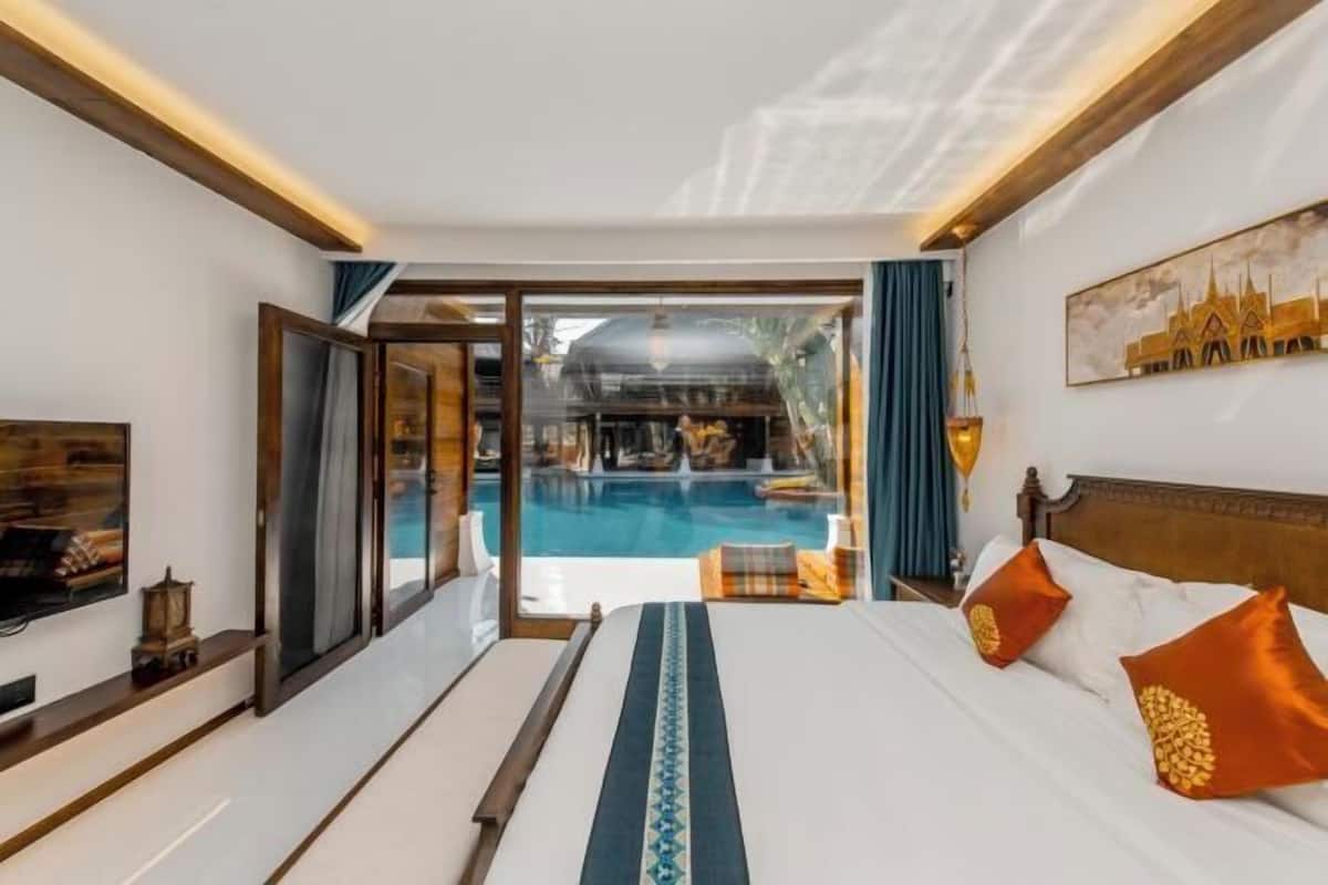 A hotel room with a bed, a television, a view of a swimming pool, and a large window.