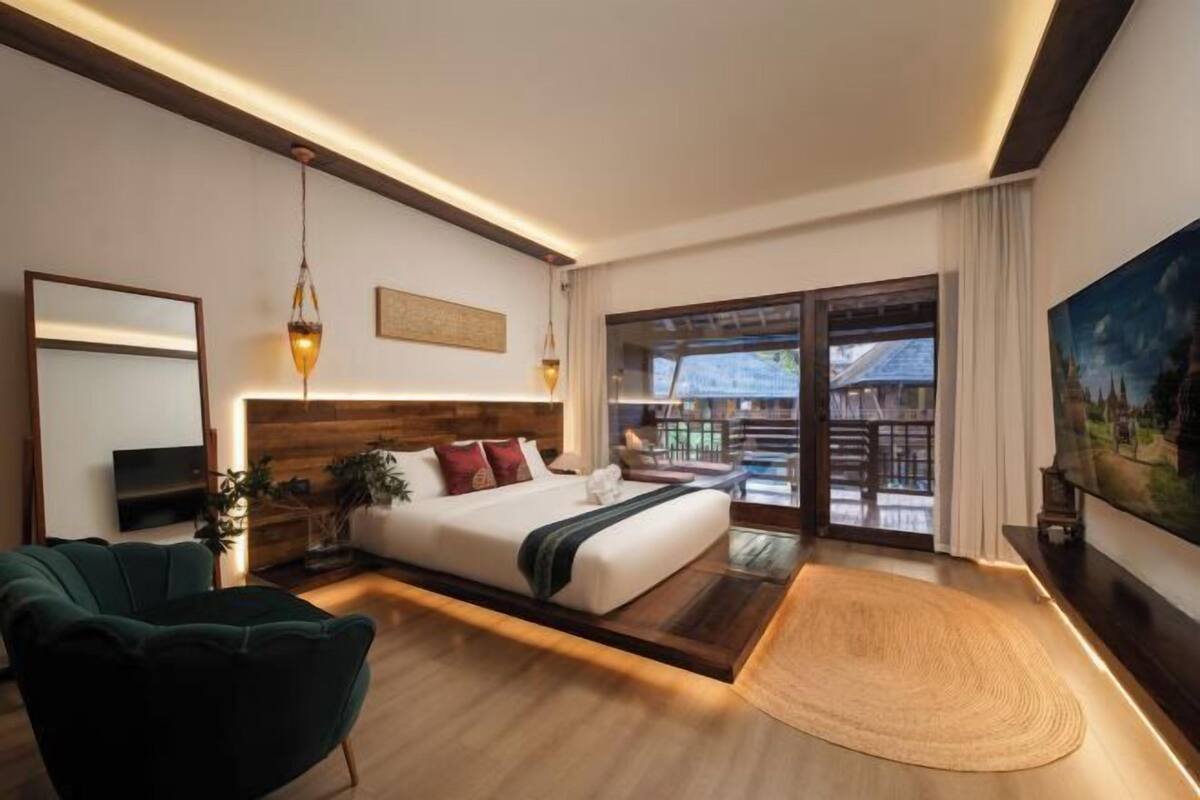 A modern hotel room with a large bed, a television, a desk, and a view of the outside.