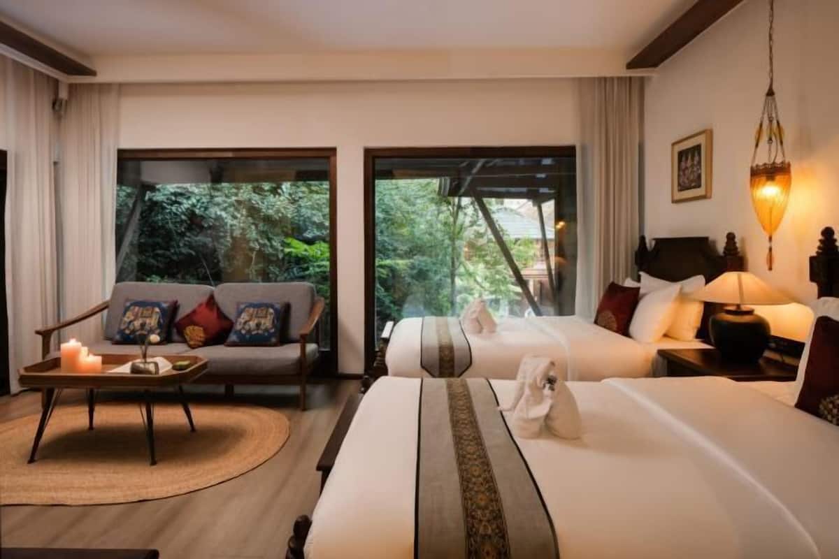 A hotel room with a bed, a sofa, a coffee table, and a view of greenery outside.