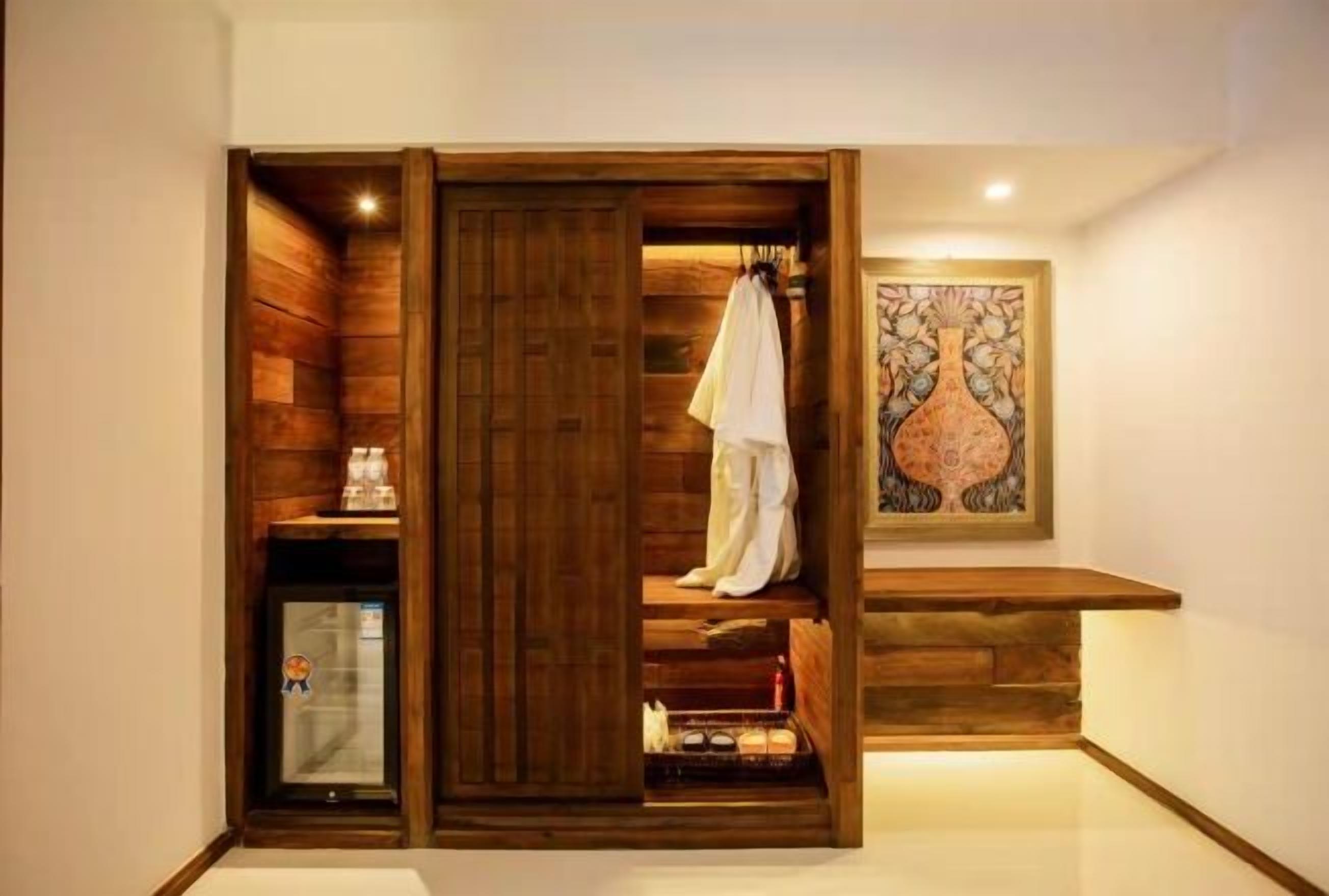A wooden wardrobe with a sliding door, a small refrigerator, and a framed artwork on the wall.