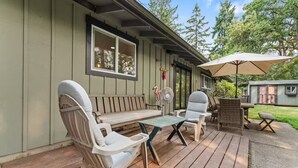 Eine überdachte Terrasse mit Holzdeck, einer gepolsterten Bank, zwei Stühlen, einem Tisch und einem Sonnenschirm.