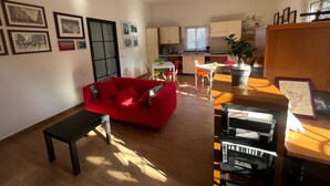 A living room with a red sofa, a coffee table, and a bookshelf. There is a kitchen area with a dining table and chairs. - Domus Joannina B&B (Pompei)